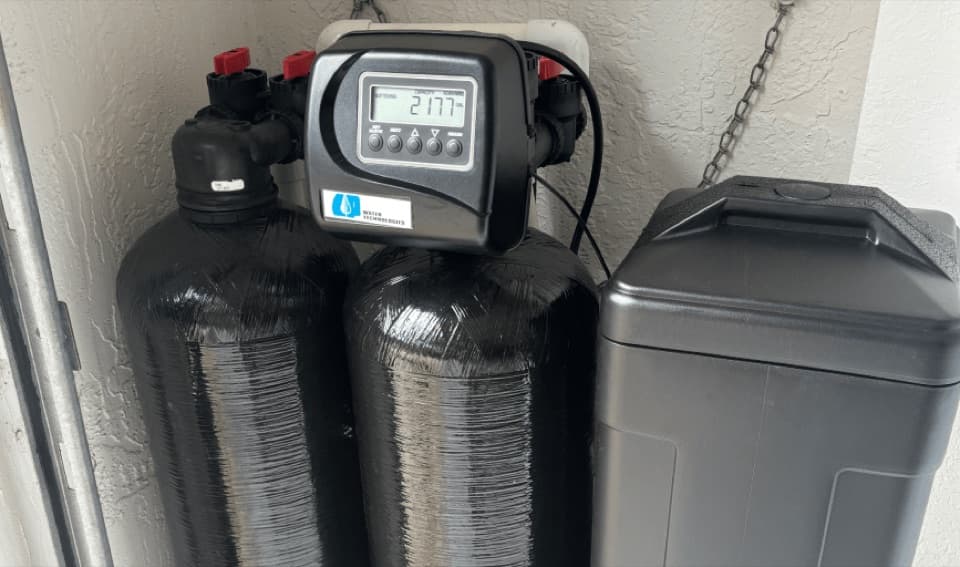 Twin black resin tanks with a digital control head, next to a grey lidded tank, against a stucco corner