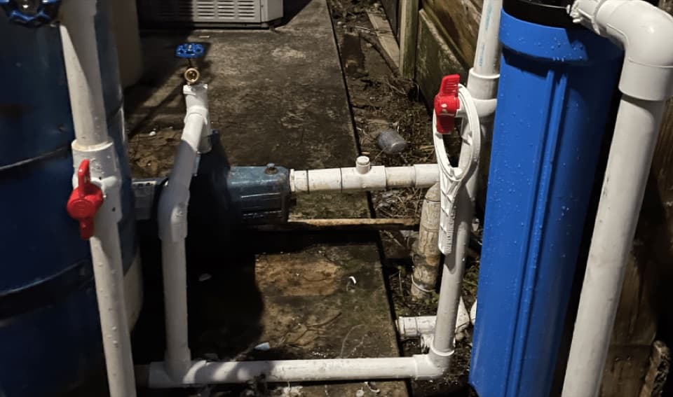 Blue motor pump joined by white PVC fittings with red valve handles, between a dark tank and a blue cartridge housing