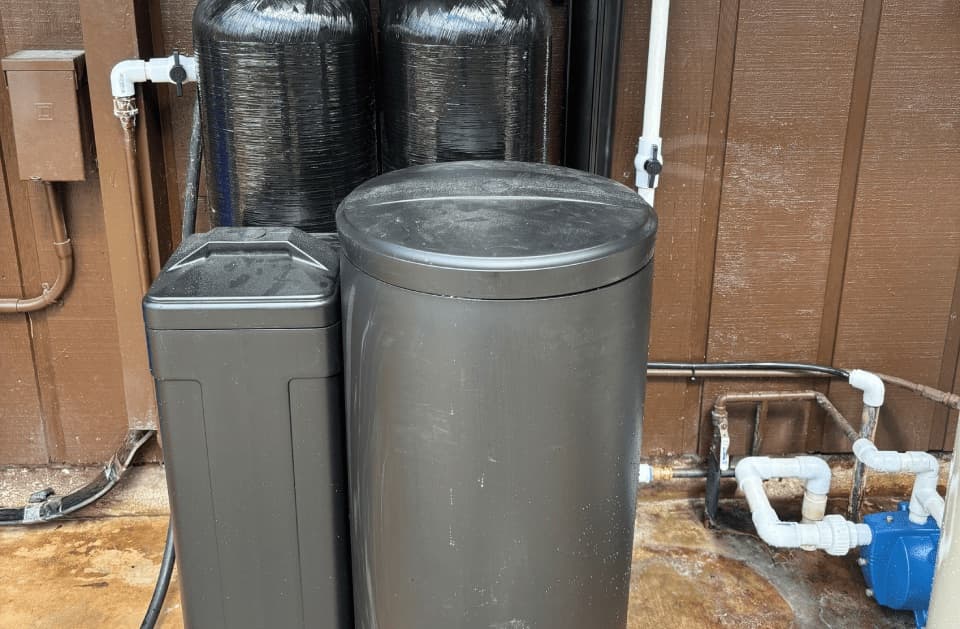 Two black tanks and two grey cylindrical tanks with lids against a wood panelled wall, with a blue pump at right
